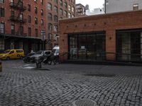 a cobble stone sidewalk with some parked cars and buildings in the background by a street hydrant