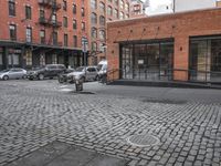 a cobble stone sidewalk with some parked cars and buildings in the background by a street hydrant