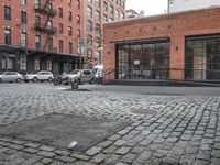 a cobble stone sidewalk with some parked cars and buildings in the background by a street hydrant