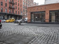 a cobble stone sidewalk with some parked cars and buildings in the background by a street hydrant