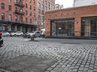 a cobble stone sidewalk with some parked cars and buildings in the background by a street hydrant