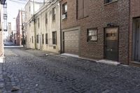a brick street with a stone sidewalk and brick buildings, two garages on either side of the lane