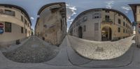 a spherical view is seen here of a narrow street between some tall buildings with cobbles and a red and white sign