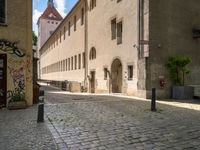 a cobblestone street in front of a tall building in a european town there is graffiti on the walls