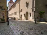 a cobblestone street in front of a tall building in a european town there is graffiti on the walls