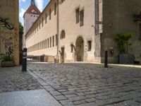 a cobblestone street in front of a tall building in a european town there is graffiti on the walls