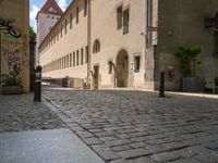 a cobblestone street in front of a tall building in a european town there is graffiti on the walls