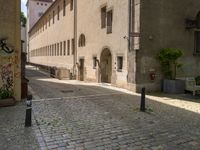 a cobblestone street in front of a tall building in a european town there is graffiti on the walls