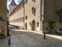 a cobblestone street in front of a tall building in a european town there is graffiti on the walls