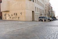 a very wide bricked street that runs past an urban area with a building and cars