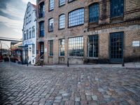 two tall buildings in a narrow alley with cobblestone street below it and a tree in front