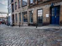 two tall buildings in a narrow alley with cobblestone street below it and a tree in front