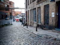 two tall buildings in a narrow alley with cobblestone street below it and a tree in front