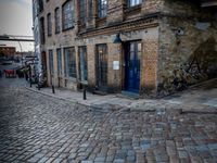 two tall buildings in a narrow alley with cobblestone street below it and a tree in front