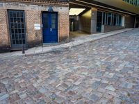 two tall buildings in a narrow alley with cobblestone street below it and a tree in front