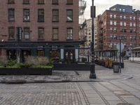 the sidewalk on a brick city street has many potted plants and small potted trees