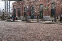 a cobblestone street with some brick buildings in the background and street lights on the side