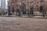 a cobblestone street with some brick buildings in the background and street lights on the side