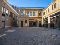 an empty brick paved building surrounded by buildings and businesses on a street corner at the center of a square