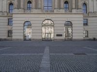 a courtyard of a building that has windows with some brickwork on the ground and a clock in front of it