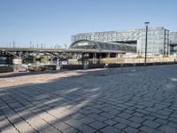 a brick courtyard with a bridge and walkway in the background that is next to a large building