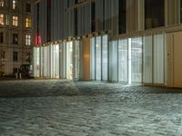 a building in the middle of a brick street at night with people sitting outside it