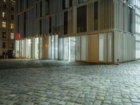 a building in the middle of a brick street at night with people sitting outside it