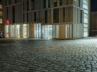 a building in the middle of a brick street at night with people sitting outside it