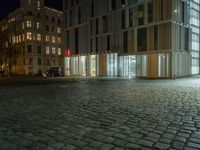 a building in the middle of a brick street at night with people sitting outside it