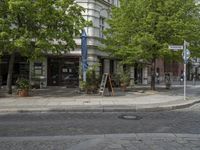 a paved road with a sidewalk in front of a store and trees in a city