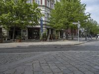 a paved road with a sidewalk in front of a store and trees in a city