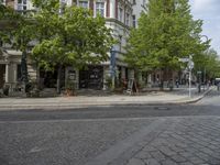 a paved road with a sidewalk in front of a store and trees in a city