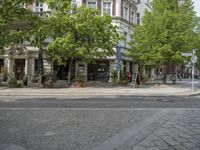 a paved road with a sidewalk in front of a store and trees in a city