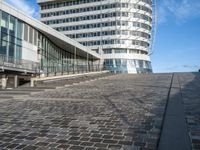 a person on a bike rides past an office building and stairs on a brick surface