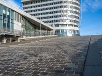 a person on a bike rides past an office building and stairs on a brick surface