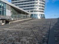 a person on a bike rides past an office building and stairs on a brick surface