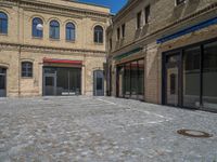 the sidewalk is paved with stones and has a bench in front of it, with no people inside