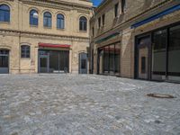 the sidewalk is paved with stones and has a bench in front of it, with no people inside