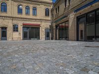 the sidewalk is paved with stones and has a bench in front of it, with no people inside