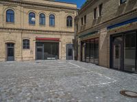 the sidewalk is paved with stones and has a bench in front of it, with no people inside