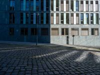 street lights and windows in front of a large building in the city by itself on cobblestone ground