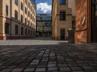 a sidewalk with chairs next to the brick building on the side, some have stairs and some buildings in the background