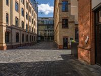 a sidewalk with chairs next to the brick building on the side, some have stairs and some buildings in the background