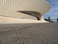 a person is walking across some cobblestones outside a building that has a curved facade