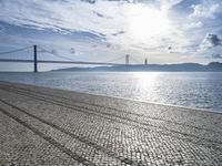 a road in front of a body of water next to a bridge and some clouds