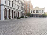 an empty bricked driveway in front of a large building with buildings along the street