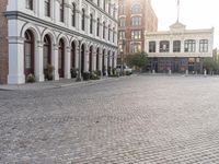 an empty bricked driveway in front of a large building with buildings along the street