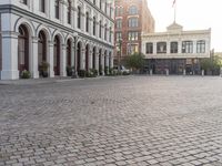 an empty bricked driveway in front of a large building with buildings along the street