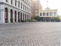 an empty bricked driveway in front of a large building with buildings along the street