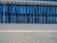 a building with pink glass and purple striped exterior is shown with the brick path on the left